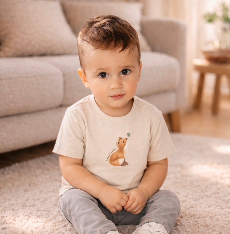Kleiner Junge trägt ein beiges Kurzarm T Shirt mit Fuchs Motiv und sitzt auf einem weichen Teppich in einem gemütlichen Wohnzimmer